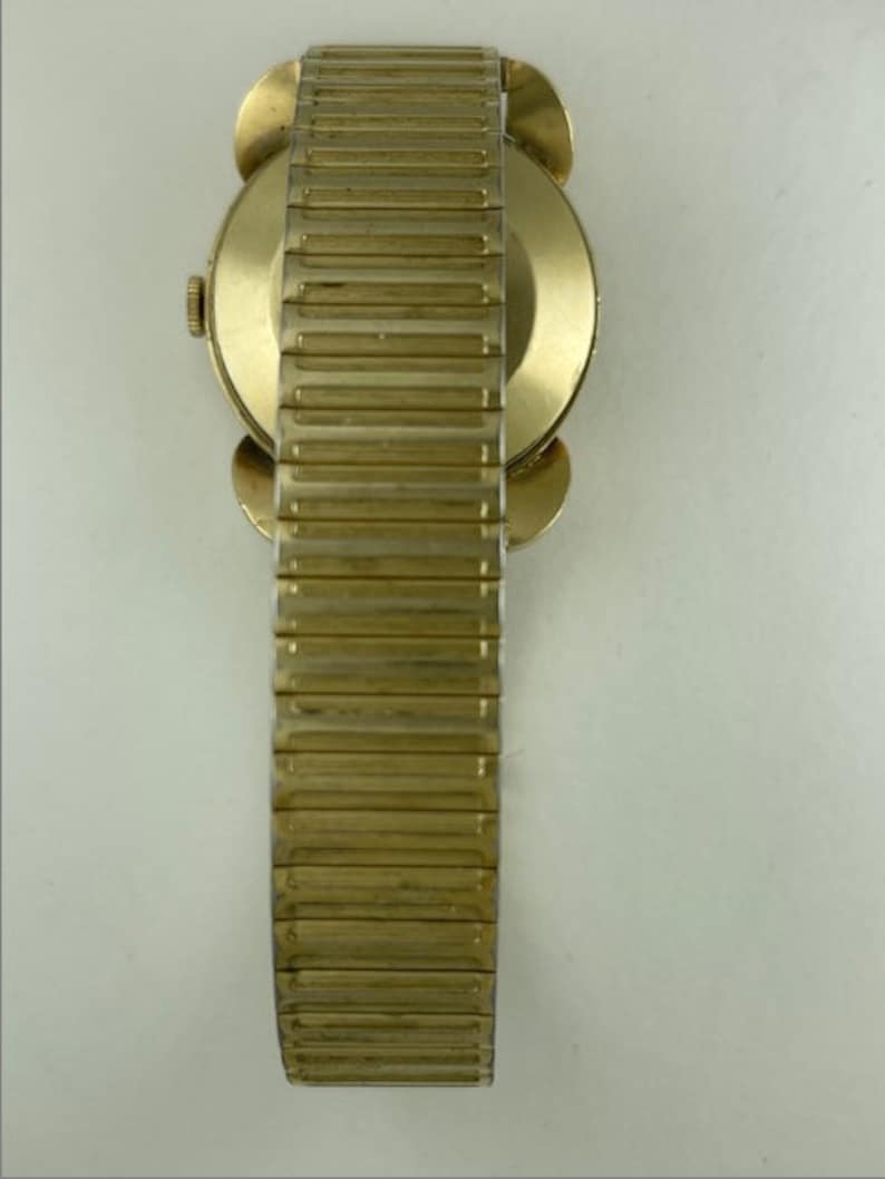 May include: A gold-toned wristwatch with a round face and a gold-toned metal band. The watch has a simple design and is in good condition.