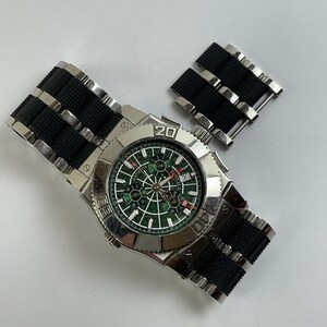 May include: A silver wristwatch with a black rubber strap and a green face. The watch features a chronograph and a date window. The watch is displayed against a white background.