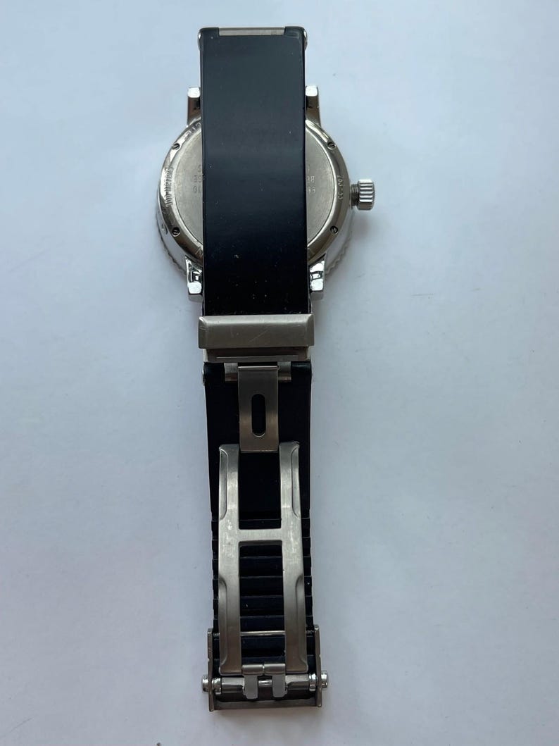 May include: A silver-toned wristwatch with a black band. The watch face is visible, and the band is open, revealing the clasp. The watch has a round face and a textured bezel.