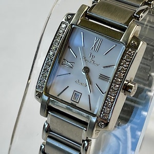 May include: A silver-toned rectangular wristwatch with a mother-of-pearl face. The watch features Roman numeral hour markers, a date display, and a diamond-studded bezel. The watch band is made of linked metal. The watch face reads "LP Pierre Pearl Quartz".
