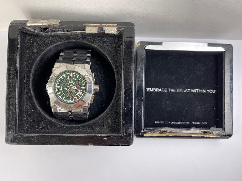 May include: A silver wristwatch with a black strap and a green face. The watch is in a black box with the words "Embrace the Beast Within You" on the lid.