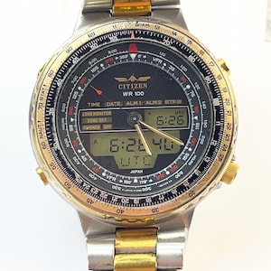 Può includere: Un orologio analogico-digitale Citizen WR 100 con bracciale a maglie in acciaio inossidabile bicolore argento e oro. Il quadrante nero presenta una lunetta con regolo calcolatore, lancette luminose e un display digitale per ora e data.