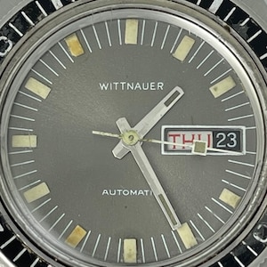 May include: A silver Wittnauer automatic watch with a gray face, black numbers, and a date window displaying "THU 23".