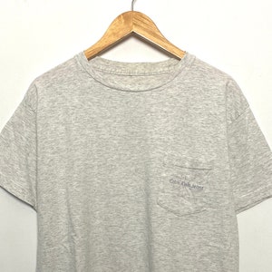 Vintage 1990s Calvin Klein Jeans Embroidered Spell Out Logo Gray Pocket Tee Shirt (size adult Large)