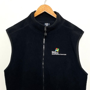Può includere: Gilet in pile nero con chiusura a zip e due tasche con zip. Il gilet ha un logo Microsoft Windows Small Business Server 2003 ricamato sul davanti.