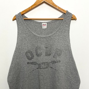 Puede incluir: Camiseta de tirantes gris sin mangas con un gráfico negro de la palabra "OCRA" con dos remos cruzados debajo.