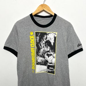 May include: Gray t-shirt with a black ringer and a graphic of Batman with the text "Doomsday Clock" in yellow.