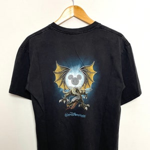 May include: Black t-shirt with a graphic of a dragon with wings and a Mickey Mouse head in a circle. The text "Walt Disney World" is printed below the graphic.