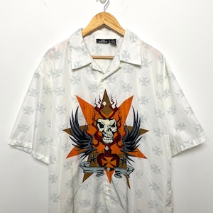May include: White short-sleeved button-up shirt with a skull and crossbones design. The design features a skull with wings, a heart, and a banner with the text "One Perfect".