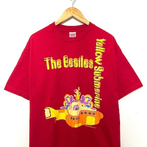 Pode incluir: Camiseta vermelha com um gráfico de submarino amarelo e o texto "The Beatles Yellow Submarine".