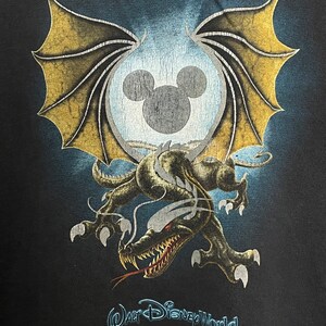 May include: Black t-shirt with a graphic of a dragon with wings and a Mickey Mouse head inside a circle. The text "Walt Disney World" is printed below the graphic.