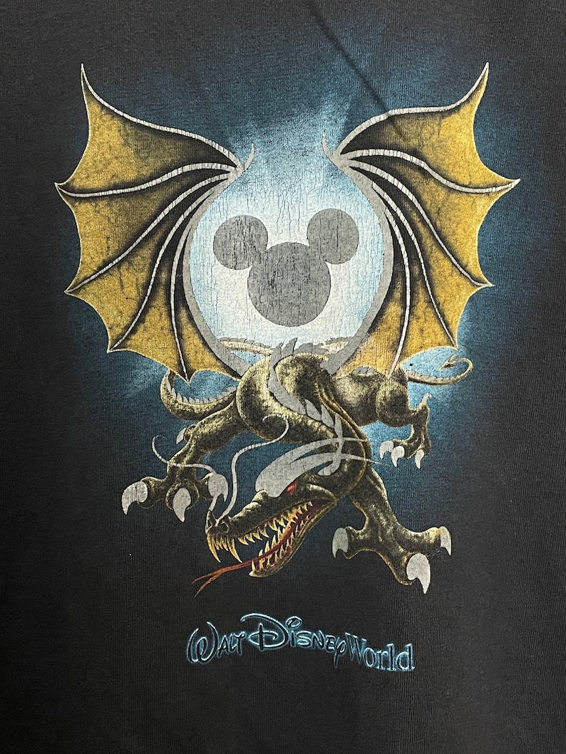 May include: Black t-shirt with a graphic of a dragon with wings and a Mickey Mouse head inside a circle. The text "Walt Disney World" is printed below the graphic.