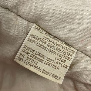 May include: A close-up of a clothing label detailing the materials used. The shell is 65% wool and 35% rayon/viscose. The insulation is polyester, the body lining is cotton, and the sleeve lining is nylon. The trim is genuine leather.