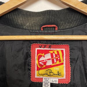 Puede incluir: Una chaqueta de cuero roja y negra con una etiqueta roja que dice "Carl Banks" y "VIR" en letras blancas. La etiqueta tambi&eacute;n dice "Made in China, Hecho en China, Fait en Chine" y "L/G".
