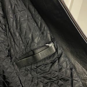 May include: Close-up of the inside of a black leather jacket. The lining is quilted and has a zippered pocket.