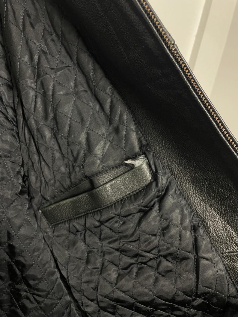 May include: Close-up of the inside of a black leather jacket. The lining is quilted and has a zippered pocket.