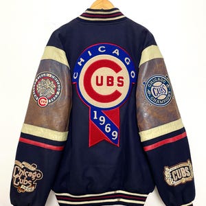 May include: Navy blue Chicago Cubs varsity jacket with leather sleeves. Features multiple patches including "CUBS" in a circular design, "1969", and "World Series Chicago Cubs 1908". The jacket has red, white, and tan accents.