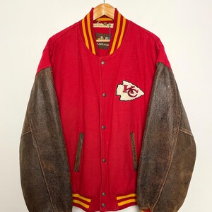 May include: A vintage letterman jacket in red and brown, with a snap-button closure. It has brown leather sleeves and a red body with yellow and red striped trim. A team logo patch is on the chest.