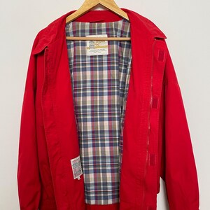 Peut inclure: Une veste rouge avec une doublure &agrave; carreaux. La veste a une fermeture &eacute;clair et un col boutonn&eacute;. L'&eacute;tiquette sur la veste indique "London Fog".