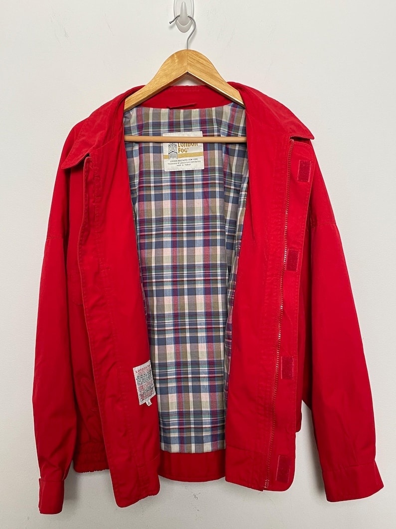 Peut inclure: Une veste rouge avec une doublure &agrave; carreaux. La veste a une fermeture &eacute;clair et un col boutonn&eacute;. L'&eacute;tiquette sur la veste indique "London Fog".