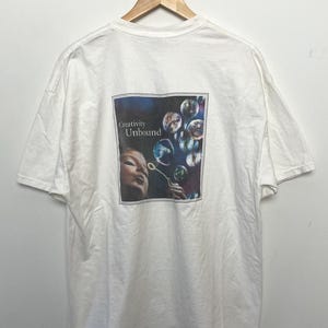 May include: White t-shirt with a graphic of a woman blowing bubbles. The graphic has the text "Creativity Unbound".