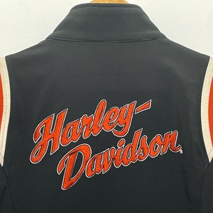 May include: Black jacket with orange and white stripes on the sleeves. The back of the jacket has the Harley-Davidson logo embroidered in orange.
