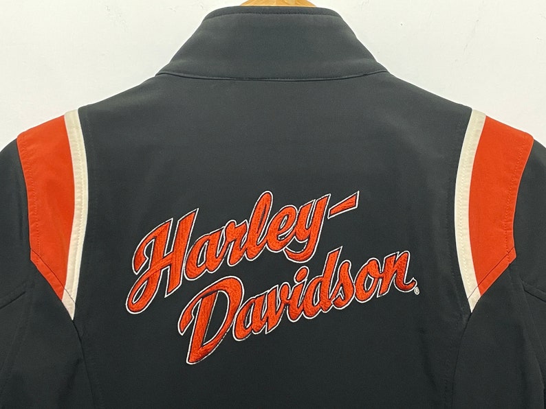May include: Black jacket with orange and white stripes on the sleeves. The back of the jacket has the Harley-Davidson logo embroidered in orange.