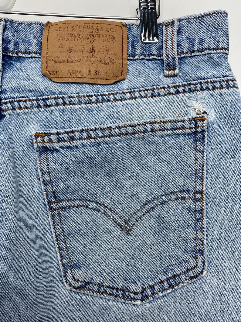 May include: Close-up of light blue denim jeans with a back pocket and a brown leather Levi Strauss & Co. label. The jeans have a waist size of 36 inches and a length of 30 inches.