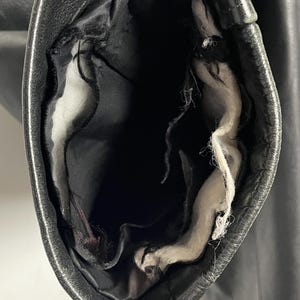 May include: Close-up of the inside of a black leather jacket sleeve. The lining is white and has some loose threads.