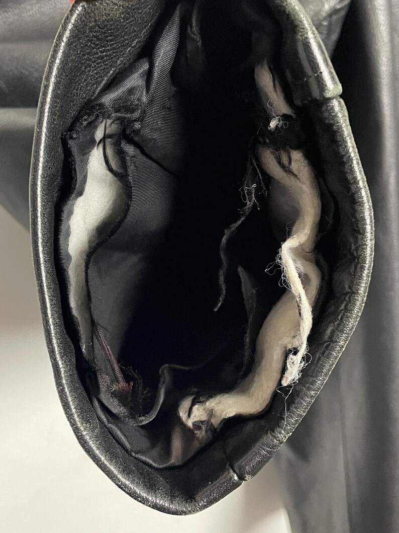 May include: Close-up of the inside of a black leather jacket sleeve. The lining is white and has some loose threads.