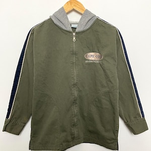 Puede incluir: Una chaqueta verde con capucha y rayas blancas y negras en las mangas. La chaqueta tiene una cremallera y un logotipo que dice "Cape Cod Massachusetts" en la parte delantera.