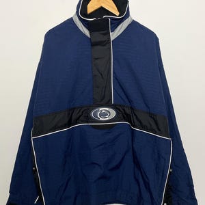 Puede incluir: Una chaqueta cortavientos azul y negra con una cremallera blanca y un logotipo de Penn State Nittany Lions en la parte delantera.