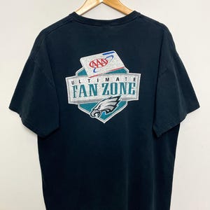 May include: Black t-shirt with a green and white graphic of the Philadelphia Eagles logo and the text "Ultimate Fan Zone" with the AAA logo.