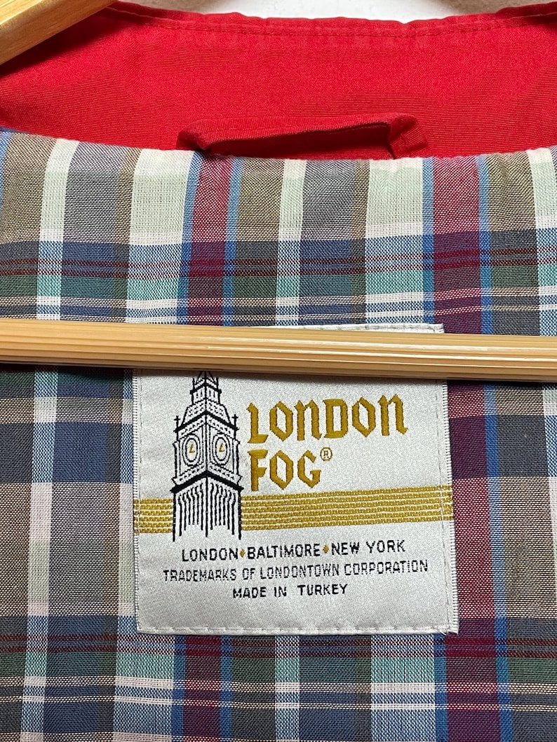 Peut inclure: Une &eacute;tiquette blanche avec des lettres dor&eacute;es qui lisent "London Fog" avec une image stylis&eacute;e du Big Ben. L'&eacute;tiquette comprend &eacute;galement le texte "London, Baltimore, New York, Trademarks of Londontown Corporation, Made in Turkey."