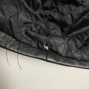 May include: Close-up of the black leather lining of a jacket, showing the stitching and a small tear in the fabric.