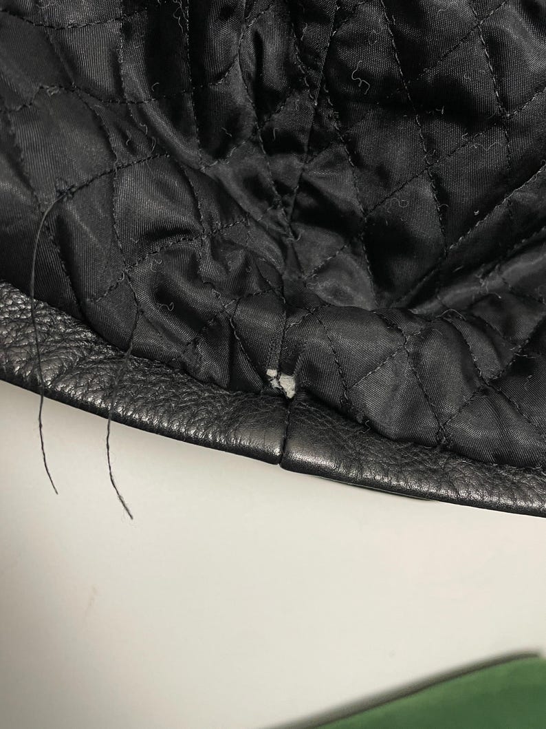 May include: Close-up of the black leather lining of a jacket, showing the stitching and a small tear in the fabric.