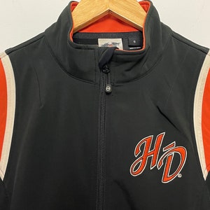 May include: Black zippered jacket with orange and white stripes on the sleeves. The jacket has a large "HD" logo on the front.