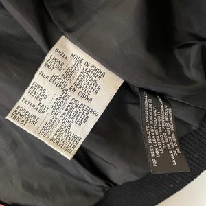 Puede incluir: Una chaqueta de cuero negra con forro rojo. La etiqueta indica que la chaqueta est&aacute; hecha en China y est&aacute; compuesta de cuero, poli&eacute;ster y acr&iacute;lico.