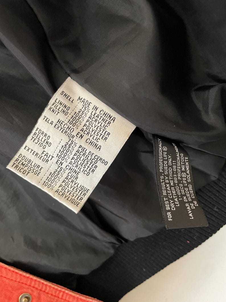 Puede incluir: Una chaqueta de cuero negra con forro rojo. La etiqueta indica que la chaqueta est&aacute; hecha en China y est&aacute; compuesta de cuero, poli&eacute;ster y acr&iacute;lico.