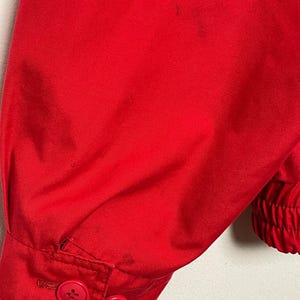Peut inclure: Gros plan sur la manche rouge d'une veste avec deux boutons. La manche a une poigne de poignet &eacute;lastique c&ocirc;tel&eacute;e.