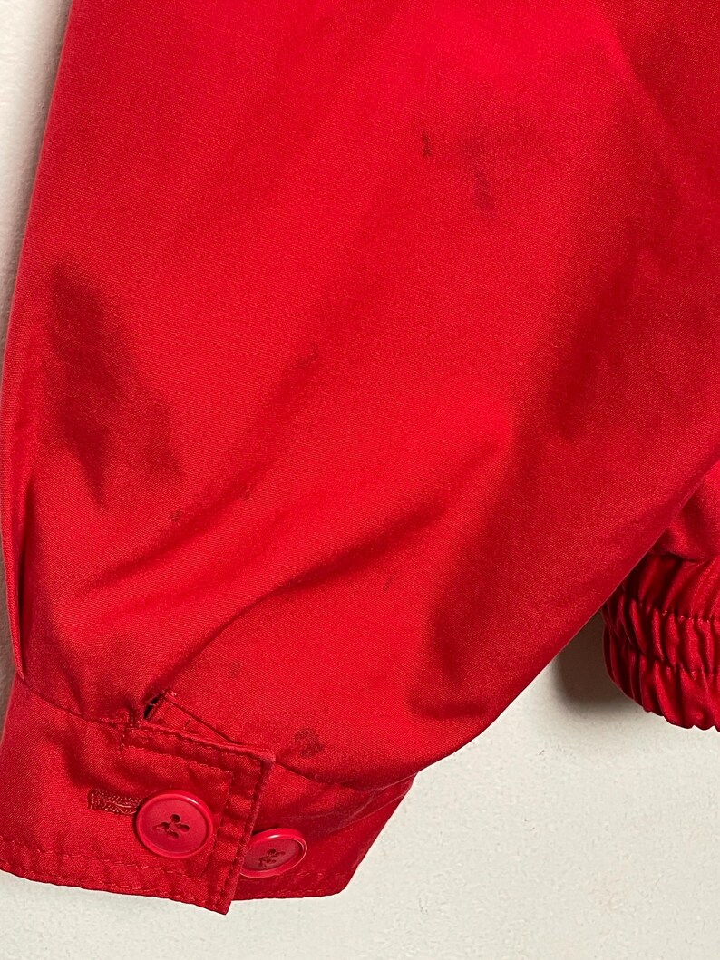 Peut inclure: Gros plan sur la manche rouge d'une veste avec deux boutons. La manche a une poigne de poignet &eacute;lastique c&ocirc;tel&eacute;e.