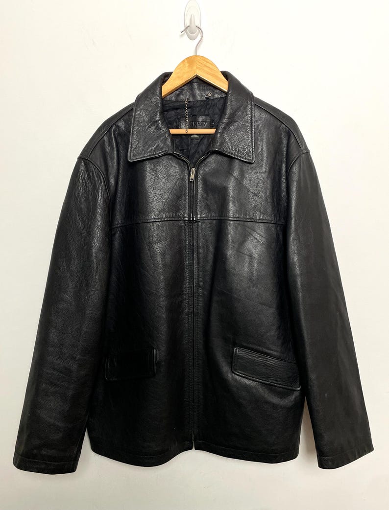 May include: A black leather jacket with a zipper closure and two pockets. The jacket has a collar and is hanging on a wooden hanger.