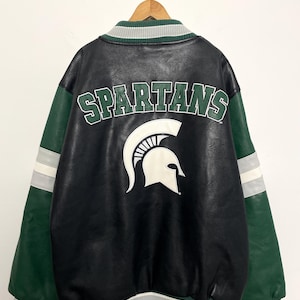 Puede incluir: Chaqueta universitaria negra y verde con la palabra "SPARTANS" y un logotipo de casco espartano en la espalda. La chaqueta tiene mangas verdes con rayas blancas y grises, y un cuello y dobladillo a rayas.