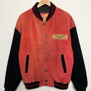 Puede incluir: Una chaqueta de b&eacute;isbol de gamuza roja y lana negra con un logotipo de Chiefs en la parte delantera. La chaqueta tiene un cuello y pu&ntilde;os a rayas rojas y negras.