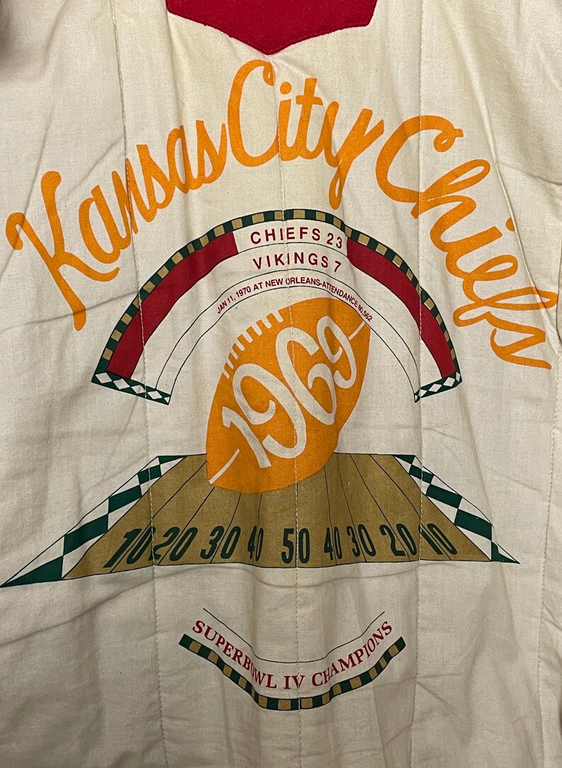 May include: Cream fabric with orange text reading "Kansas City Chiefs." The image commemorates Super Bowl IV, with the score Chiefs 23, Vikings 7, and the year 1969. Includes a football graphic and yard lines.