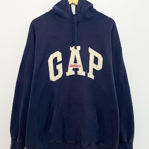 May include: Navy blue hooded sweatshirt with the word "GAP" in large, off-white, block letters across the chest. The word "Athletic" is in red script below the "GAP" logo. The sweatshirt has a front pocket and a drawstring hood.