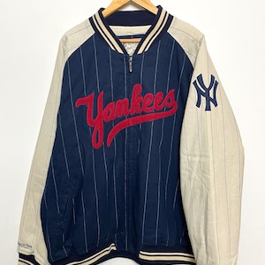 May include: A blue and white striped baseball jacket with a red embroidered "Yankees" logo on the front and a white embroidered "NY" logo on the sleeve.