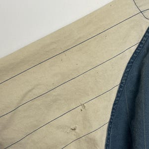 May include: A garment featuring a beige section with thin dark blue pinstripes and a solid dark blue section. The beige fabric displays two small holes in the lower portion of the striped area, showing signs of wear and fraying on the material.