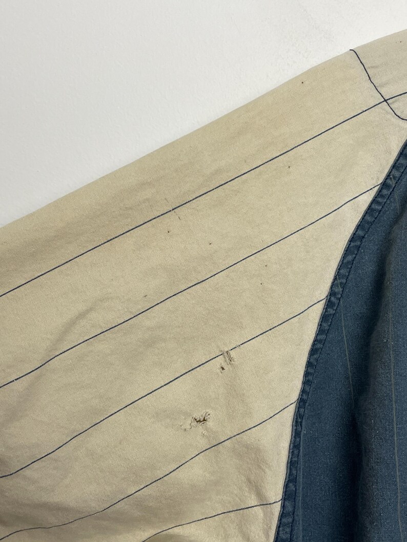 May include: A garment featuring a beige section with thin dark blue pinstripes and a solid dark blue section. The beige fabric displays two small holes in the lower portion of the striped area, showing signs of wear and fraying on the material.