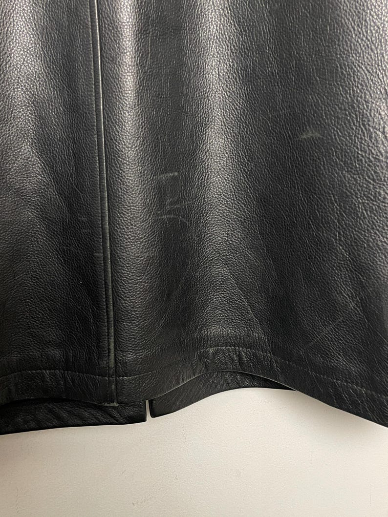 May include: Close-up of the bottom edge of a black leather jacket. The jacket has a seam down the center back and a curved hem.